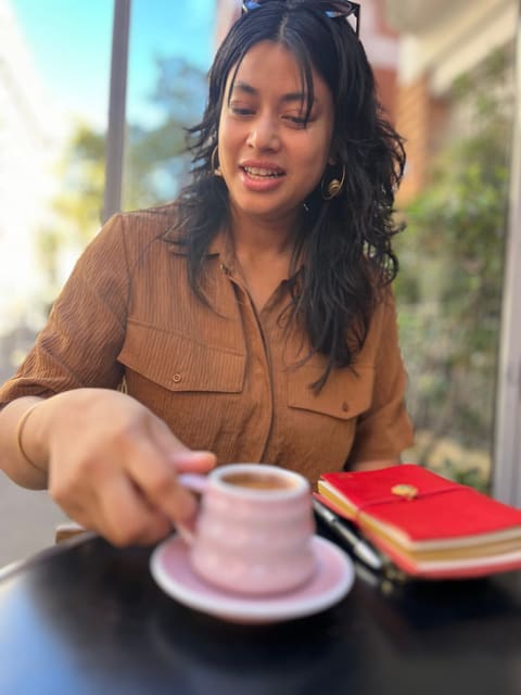 Mishar at a café table with an espresso and her red notebook